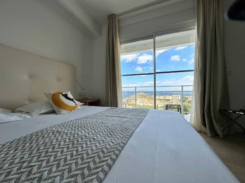 Hotel room with bed and balcony view of coastal town and blue sea