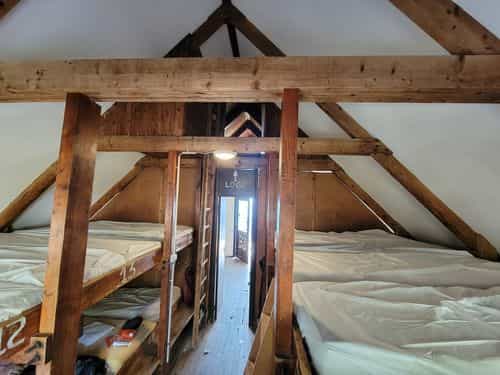 Bunk beds in a rustic attic dormitory with exposed wooden beams at Refuge de Pietra Piana.