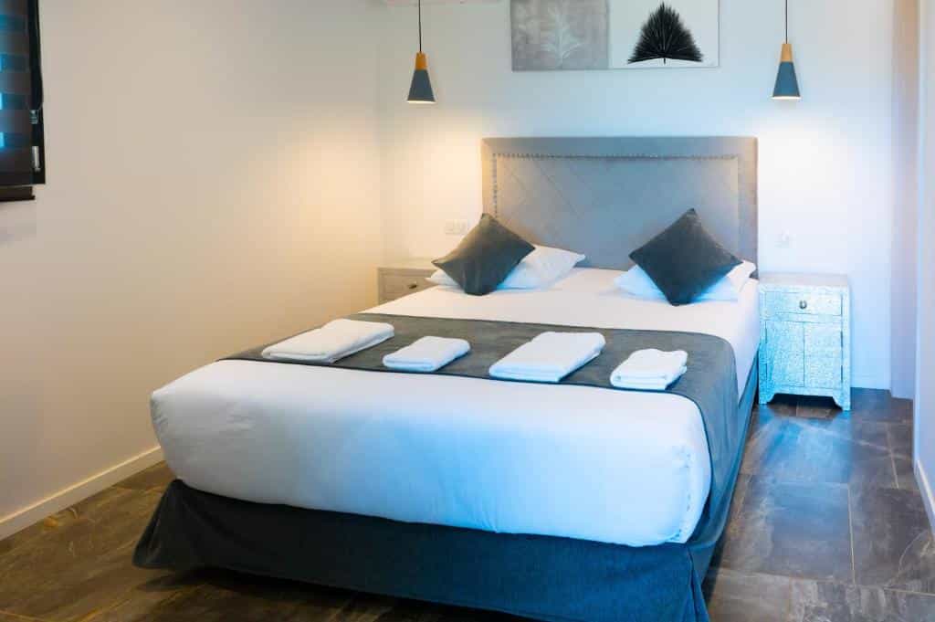 Modern hotel bedroom with large bed, white linens, dark pillows, and bedside tables.