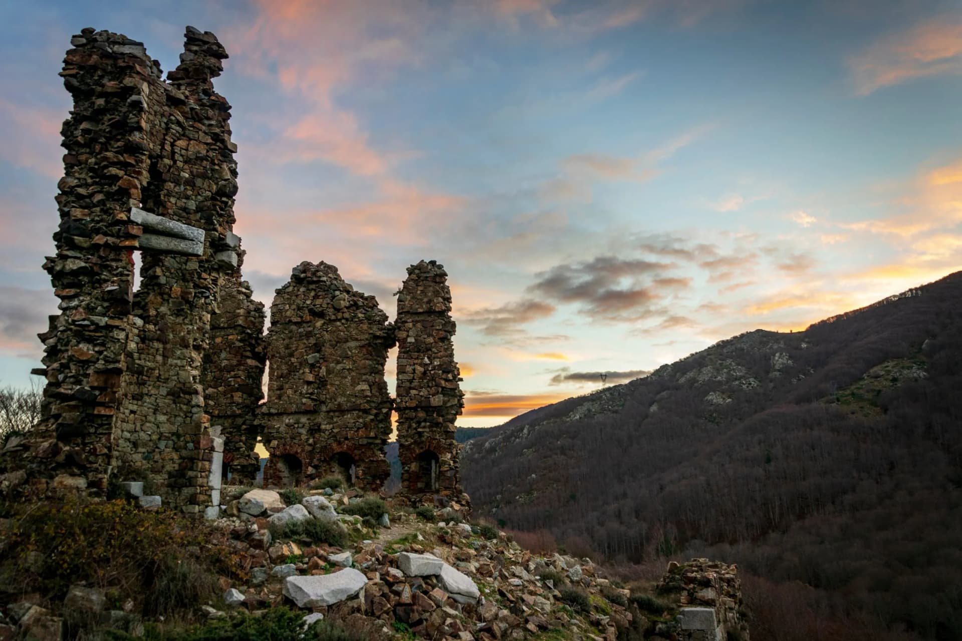 Stone ruins on a hillside overlooking a dark, wooded mountain at sunset, Col de Vizzavona, Corse.