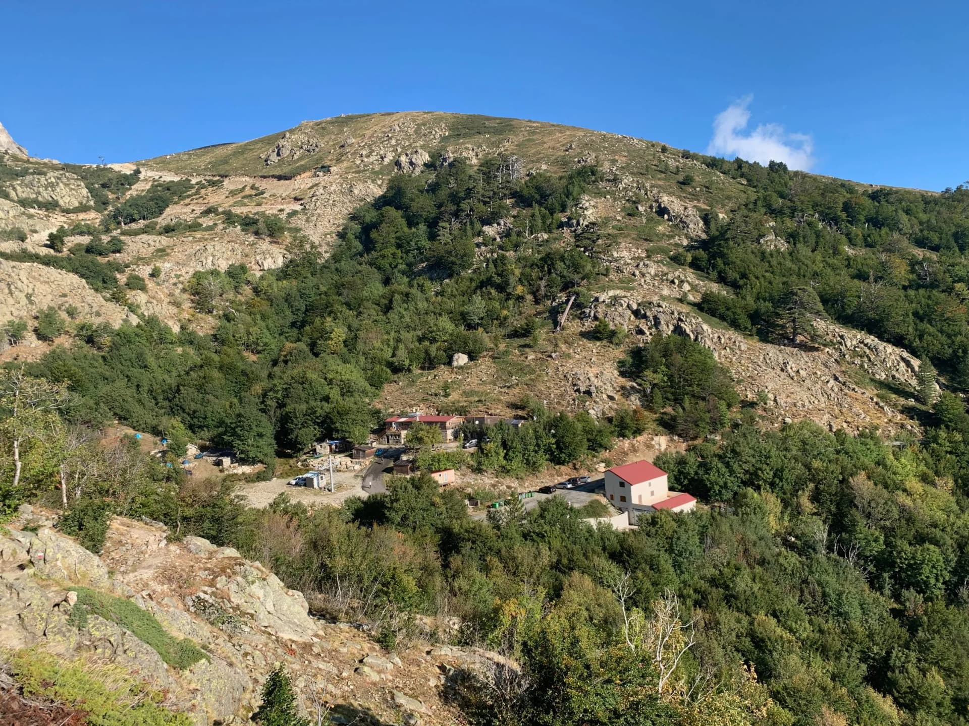 Refuge de Capannelle in Corsica, buildings nestled in a lush green mountain landscape under a clear blue sky.