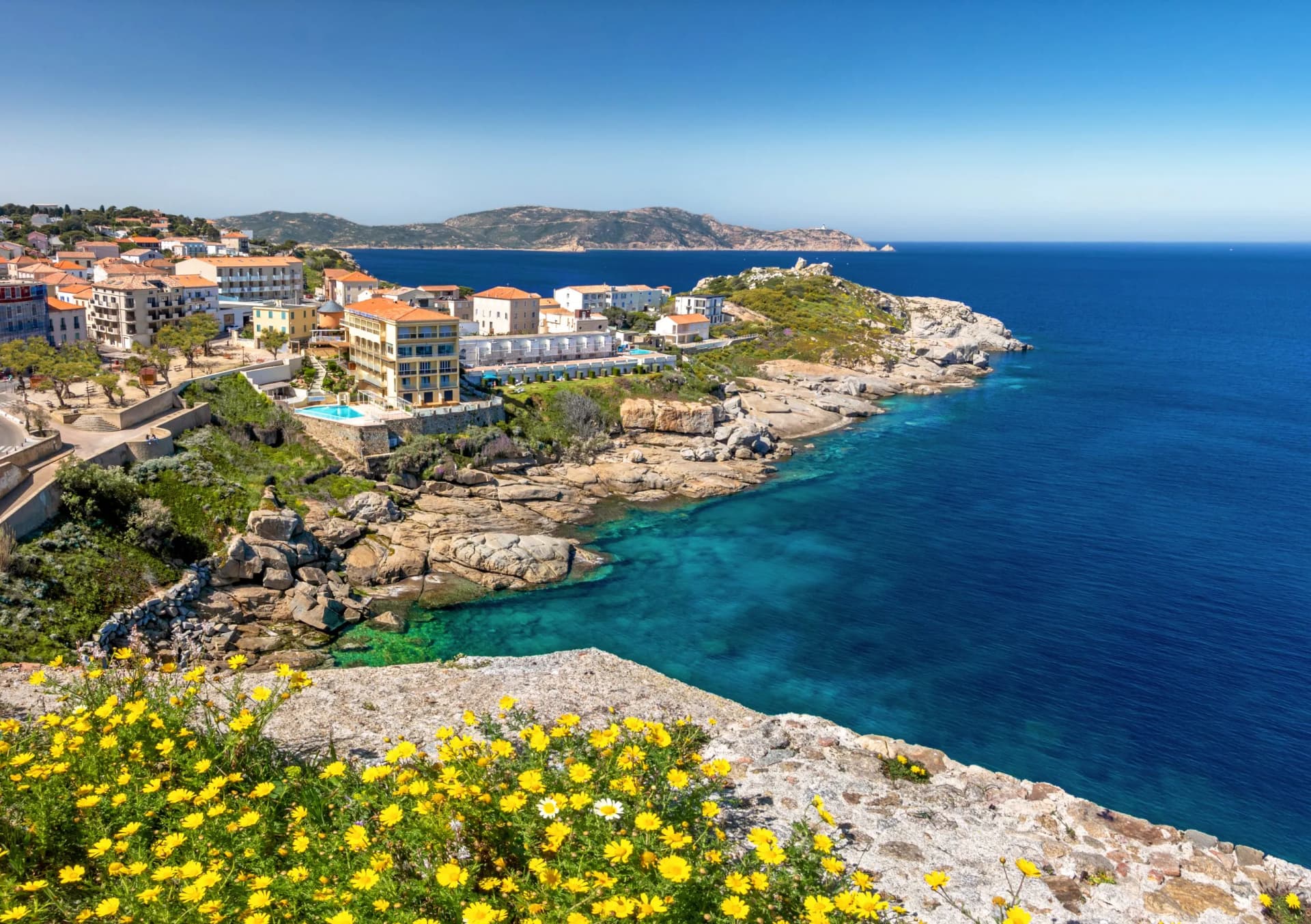 Coastal town in Calvi, Corsica with yellow flowers overlooking turquoise Mediterranean Sea